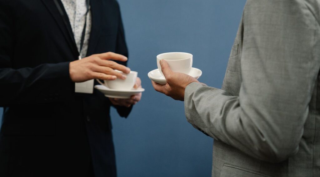 Two business professionals holding coffee cups during a casual meeting or event.